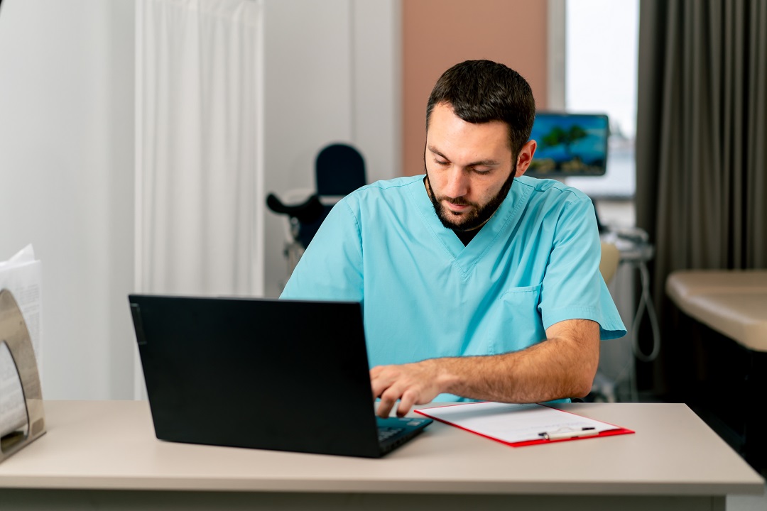 Focused male provider engaging in accurate physical therapy documentation on laptop