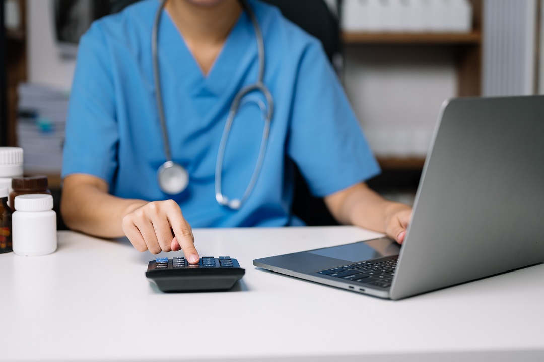 Male faceless rehab therapist performing medical coding with calculator and laptop on table